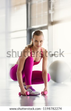 Portrait of attractive woman training with dumbbells in light modern gym