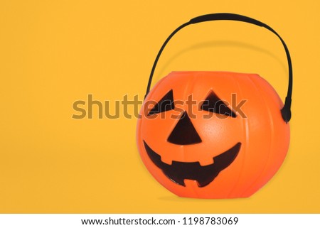 Jack O' Lantern Halloween pumpkin pail on yellow background. Orange plastic Trick Or Treat candy bucket made from resin with handle.