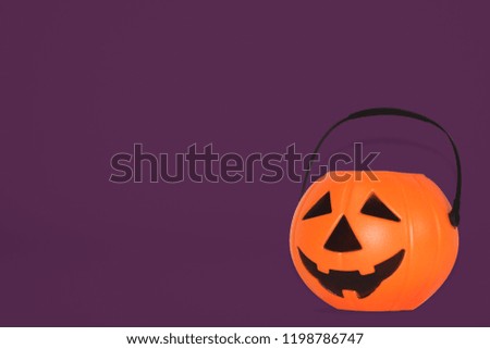 
Jack O' Lantern Halloween pumpkin pail on purple background. Orange plastic Trick Or Treat candy bucket made from resin with handle.