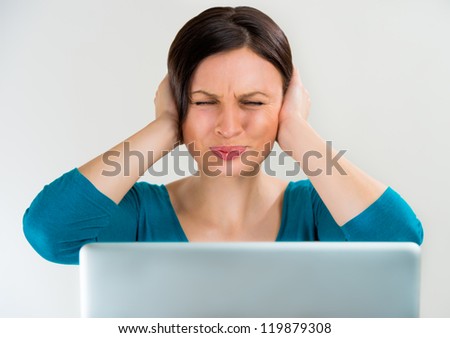 Young pretty woman with closed eyes and her covering ears sitting in front of laptop. Do not wants listen other opinions and a lot of work concept