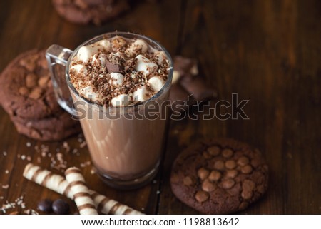 Cup of cocoa with marshmallows and chocolate chip cookies on dark wooden background.