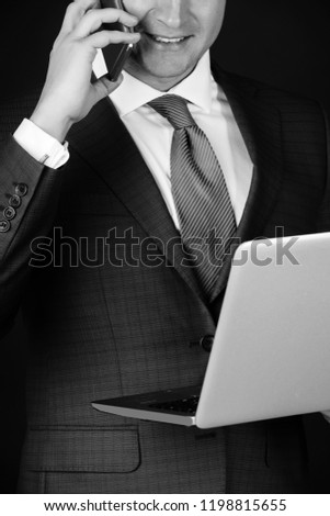 Laptop or computer in male hand. Man talking on mobile phone or smartphone on black background. Technology for business. Conversation and internet surfing