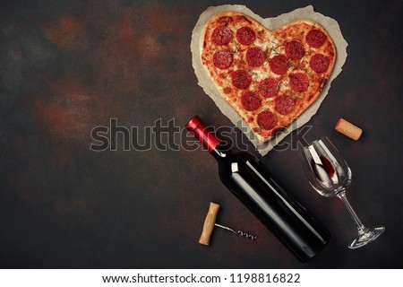 Heart shaped pizza with mozzarella, sausagered with a bottle of wine and wineglas. Valentines day greeting card on rusty background . Top view Royalty-Free Stock Photo #1198816822