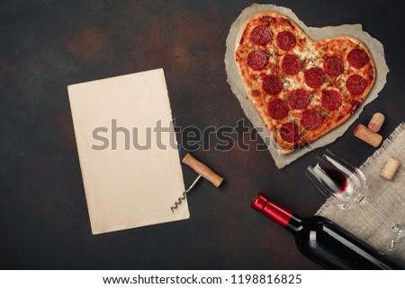 Heart shaped pizza with mozzarella, sausagered with a bottle of wine and wineglas , paper. Valentines day greeting card .  Top view with space for your text. Royalty-Free Stock Photo #1198816825