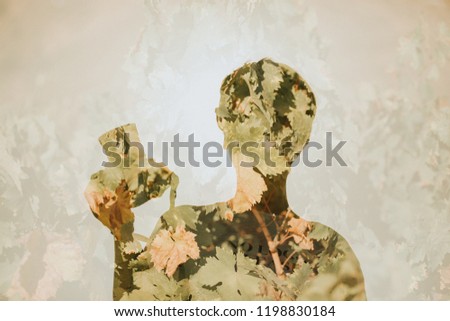 Conceptual double exposure portrait of woman holding a camera in the hand, mixed with plant leaves.