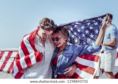 Our secret. Handsome male person holding flag while caressing his girlfriend