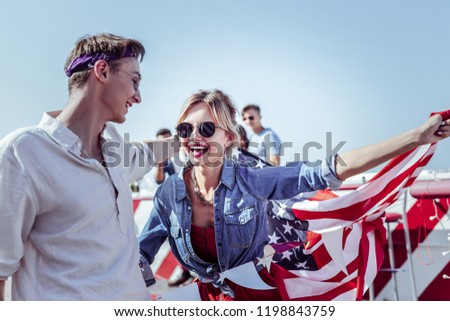 Red lipstick. Pleased girl keeping smile on her face while holding American flag