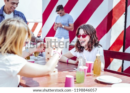 Stylish people. Charming brunette female keeping smile on her face while looking at jenga game