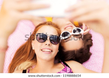 summer fashion, eyewear and leisure concept - smiling teenage girls in sunglasses lying on picnic blanket taking selfie