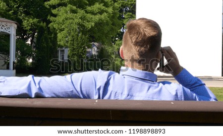 Young handsome student guy is sitting in the park on a bench, mobile phone. Concept: communication