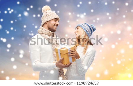 winter, holidays, couple, christmas and people concept - smiling man and woman in hats and scarf with gift box over snow background