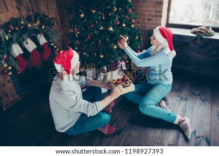 Above high angle view of two cheerful beautiful adorable lovely grey-haired married spouses husband wife granddaddy granny decorating domestic shiny fir tree with toys balls adornment