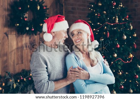 Two cheerful nice lovely sweet tender beautiful adorable grey-haired spouses husband and wife grandma granddad enfolding near eve noel shiny fir tree romantic evening date meeting
