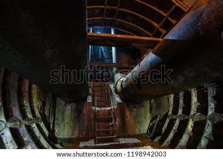 Underground tunnel with pipes and stairs to the surface.