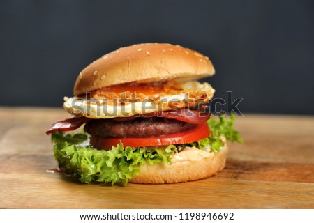 
Hamburger on a light wooden surface. The burger includes bacon, fried egg and dried onions. Close-up. Macro shooting.