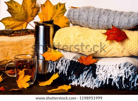 Autumn home decor.Metallic coffee pot and Glass cup  with healing tea amid bright yellow leaves on the background of knitted clothes and checkered plaid. Hygge Style, concept of comfort
