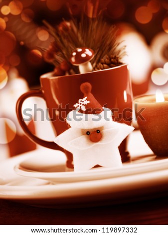 Grunge photo  of Christmastime utensil set, red tea cup standing on white plate and decorated with Santa Clause star toy, candle, fir cone and branch of Christmas tree, dark luxury xmas still life