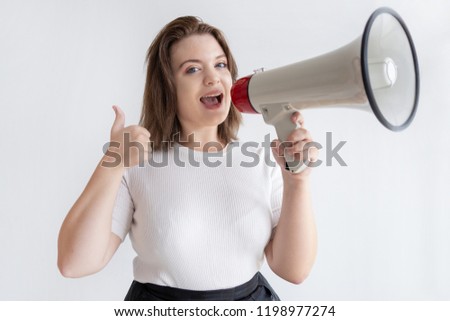 Pretty young marketing manager shouting into loudspeaker. Happy young woman making announcement and showing thumbs-up. Special offer concept