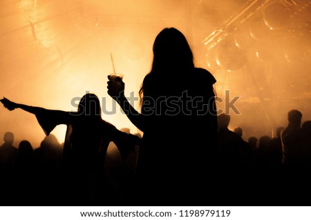 Silhouette of 2 young women dancing in a nightclub with lights in the background