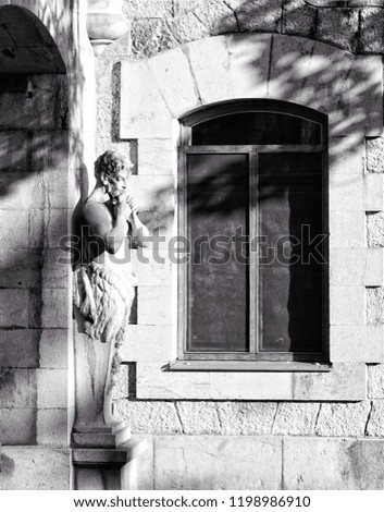 Massandra Palace, Yalta, Crimea, Russia. The royal palace with sculpture of man in full growth with his hands folded on his chest. The statue stands near old window. Shadows and lights from leaves.