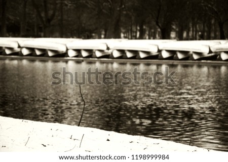 Winter park lake landscape. Closed boat station in park covered with snow. Lake Daumesnil, Paris, France. Selected focus on the snow at foreground. Sepia photo.