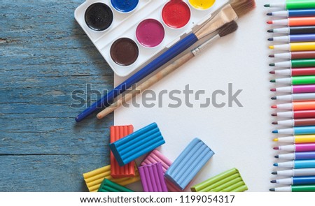 Set of watercolor paints, brushes for painting with colorful plasticine and blank white paper sheet on vintage wooden background. Top view.