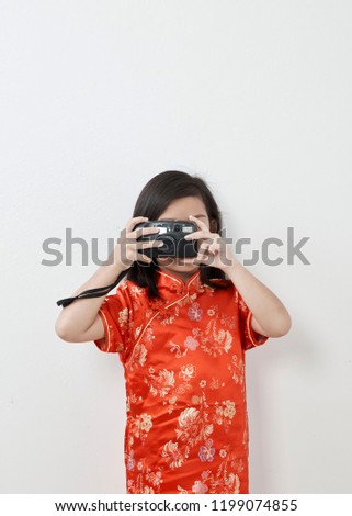 Cute little girl 8 years in Chinese dress traditional cheongsam New year 2019  takes picture with vintage retro photo camera. Doing snapshot or taking picture in red dress.