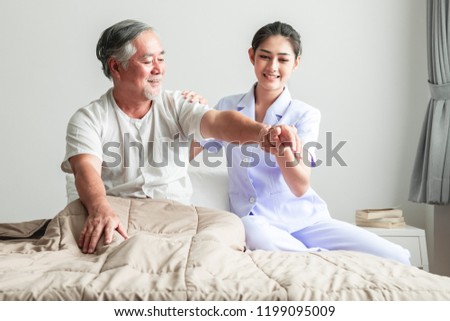 Young attractive physiotherapist working on senior man. Beautiful asian woman working with asian senior man's arm. Senior home caretaker service concept. Royalty-Free Stock Photo #1199095009