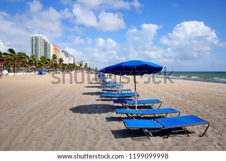 Blue lounge chairs and umbrellas line Fort Lauderdale Beach directly in front of the Atlantic Ocean. 
