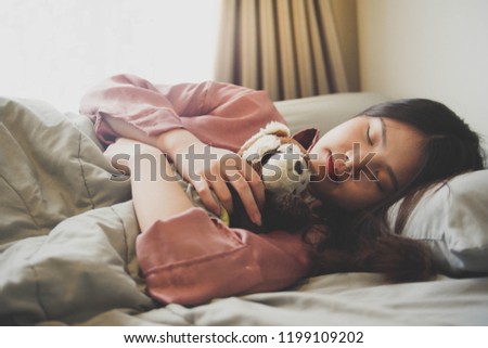 Image of an Asian woman sleeping and hugging a cute doll in bed with gray blanket , flare lighting from the window.