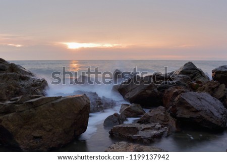 Sea waves hit the rocks at sunset.