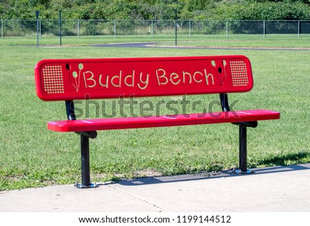 red buddy bench on a school play ground. A bench for a shy or lonely child to sit on to indicate they need a friend or a buddy Royalty-Free Stock Photo #1199144512
