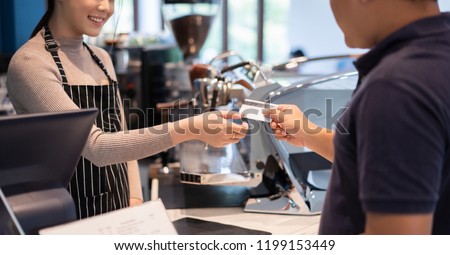 Asian women barista accept credit cards from customers in the coffee shop.