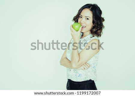 Portrait of happy young Asian woman wearing blouse standing and biting apple. Healthy eating and dieting concept