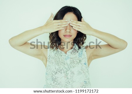 Serious calm woman covering eyes with hands while preparing to see gift. Asian girl playing hide-and-seek. Embarrassment concept