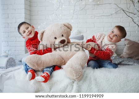 Two brothers Boy in a Christmas red sweater with a picture of a deer sitting on a bed with pillows.