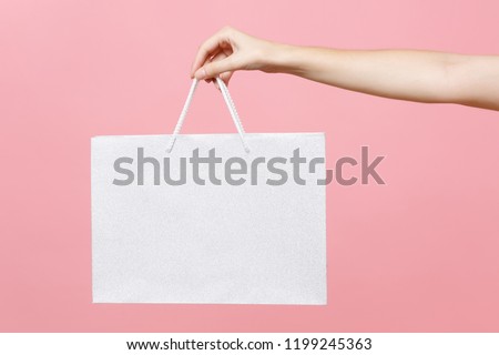 Close up female holds in hand white clear empty blank craft paper gift bag for purchases after shopping isolated on pastel pink background. Packaging template mockup. Delivery concept advertising mock Royalty-Free Stock Photo #1199245363
