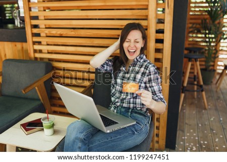 Woman in outdoors street summer coffee shop wooden cafe sitting working on laptop pc computer, hold bank credit card, relaxing during free time. Mobile Office. Lifestyle freelance business concept