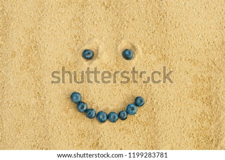 happy smiley face made from fresh blueberry on yellow sand background, bilberry are a healthy and vitamin-rich product and ingredient for healthy diets and vegetarians