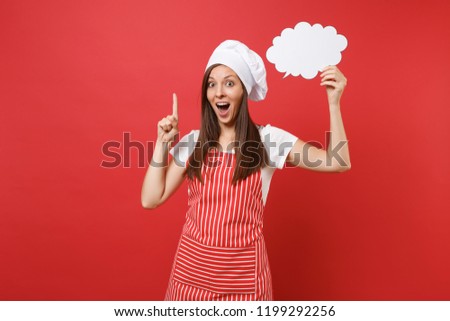 Housewife female chef cook or baker in striped apron white t-shirt toque chefs hat isolated on red wall background. Woman hold in hand empty blank Say cloud, speech bubble. Mock up copy space concept