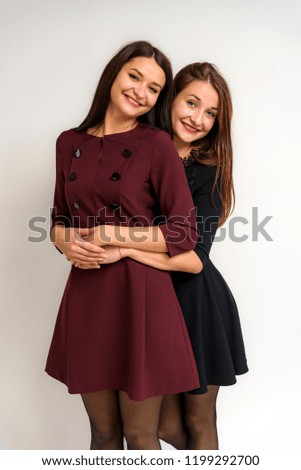 Studio portrait of beautiful brunette girls sisters on a white background in a dress with different emotions. They are standing right in front of the camera smiling and looking happy.