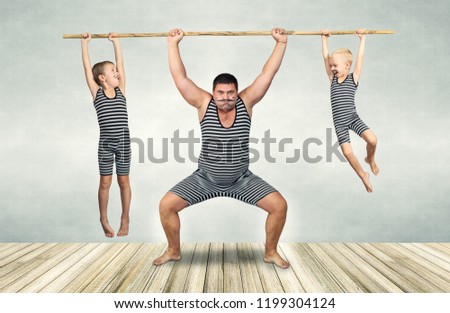 Family of strongman. The father of two sons in vintage costume of athletes perform strength exercises. Family look. Royalty-Free Stock Photo #1199304124