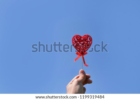 A hand holding a red valentines heart with yellow flowers on the background in springtime.
