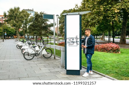 Young man renting a bicycle in a post with customizable poster outdoors