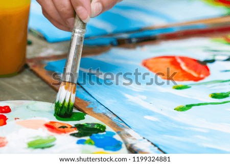 A girl paints a picture by gouache. A girl drawing poppies and chamomiles. The hand and paint brush. Closeup, selective focus