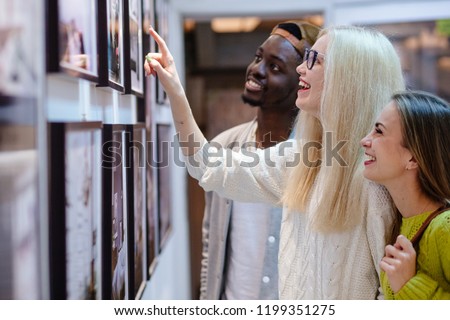 Three young people hipster students with different skins looking happy together, talkng, looking at picture on wall, spending free time together in art photo gallery. Multi ethnic, friendship concept. Royalty-Free Stock Photo #1199351275