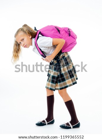 Sweet little girl in uniform carrying heavy big pink backpack or school bag full causing stress and pain on back due to overweight isolated on white background in school education concept
