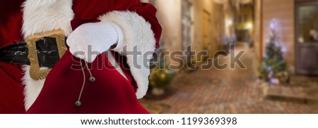 Christmas concept Santa claus standing on the streets of a small alley holding his bag full of presents