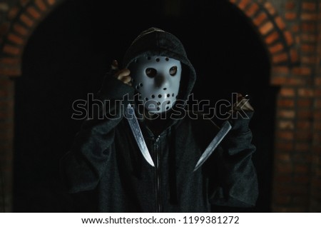 man in a hood and hockey mask with two  knifes on a black background
