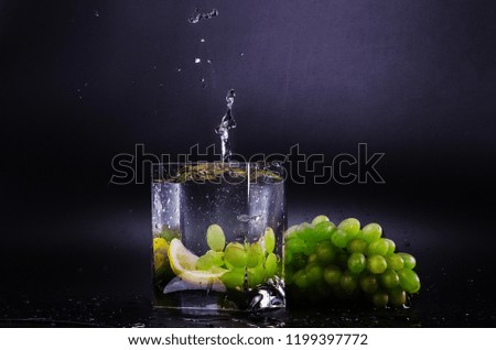 grape falls into a glass of water with large splashes on a black background. Big bunch of grapes